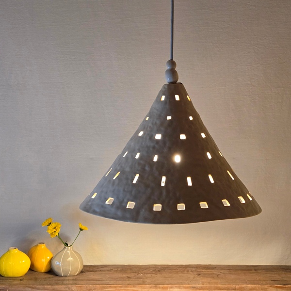 large ceramic pendant light with small cutouts shining on 3 small bud vases