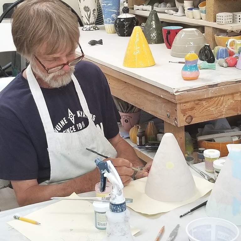man painting ceramic wares with underglazes